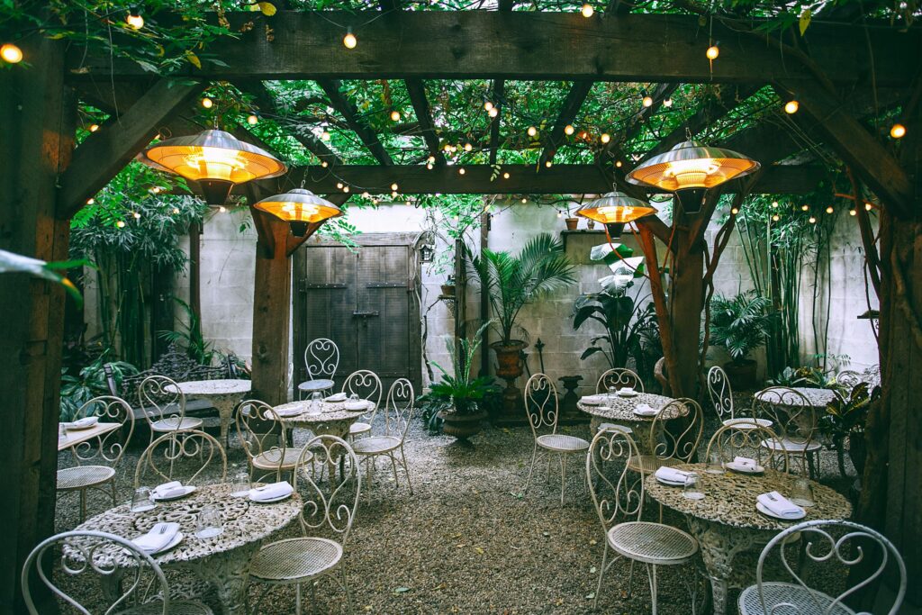 Cafe with setting on ornamental tables near chairs under decorative lamps in backyard on summer day