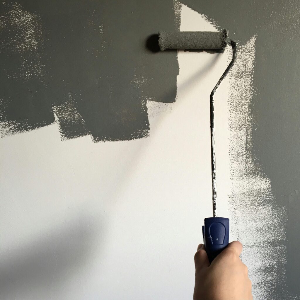 A hand painting a wall gray with a roller during a house renovation project.